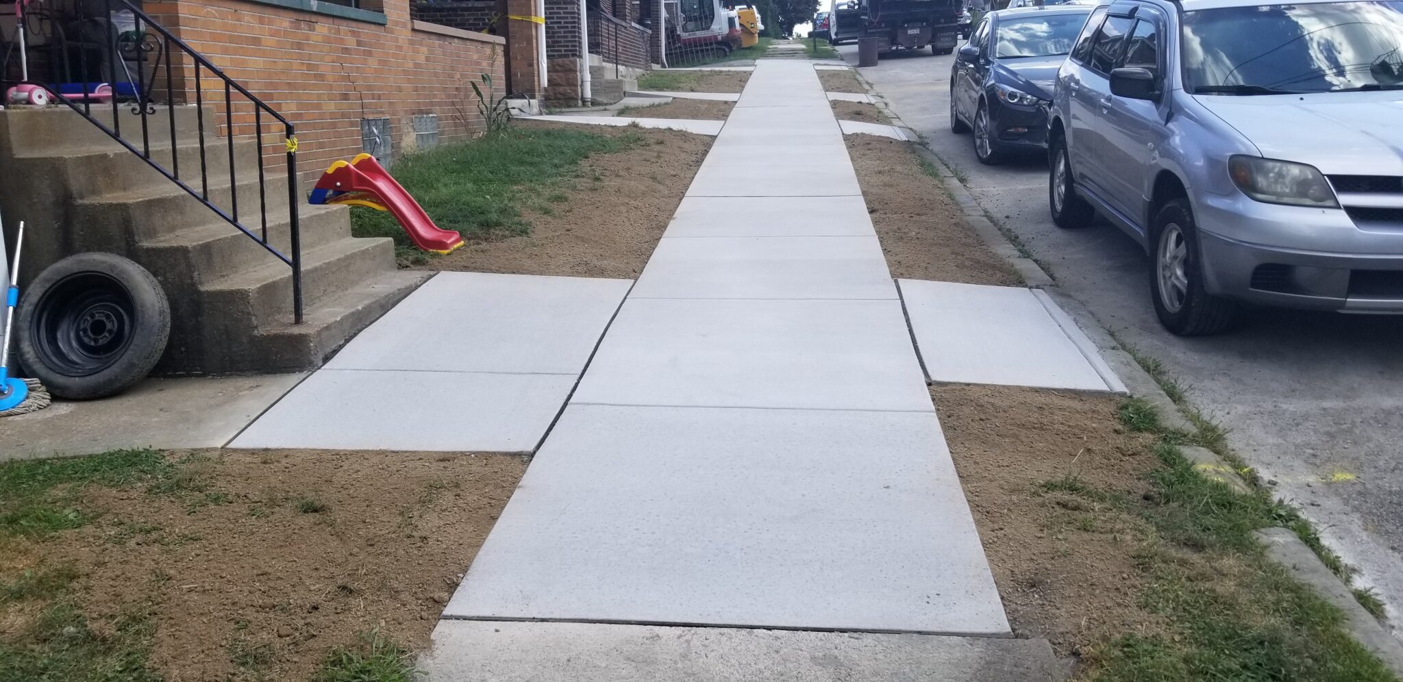 A sidewalk with cement blocks and grass on the side.