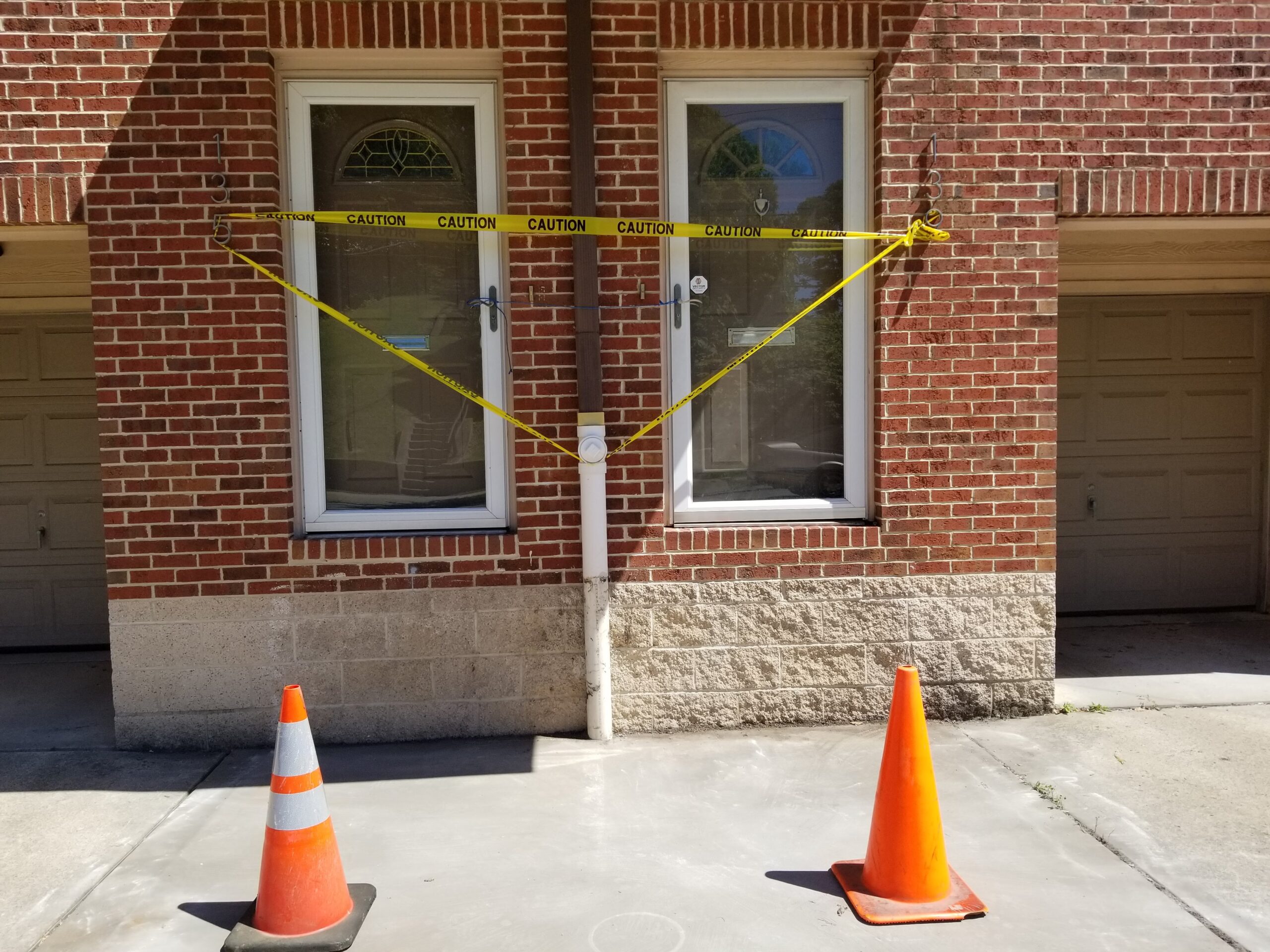 20210616_111659 A building with two orange cones and yellow caution tape.