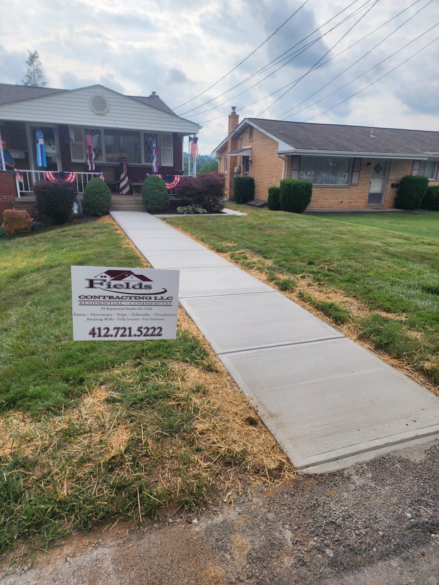 A sidewalk with grass and a house in the background.
