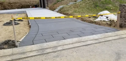 A concrete driveway with yellow caution tape blocking off the sidewalk.