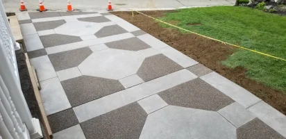 A sidewalk with a checkered pattern and grass growing on it.