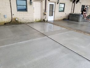 A concrete driveway with two doors and no one in it.